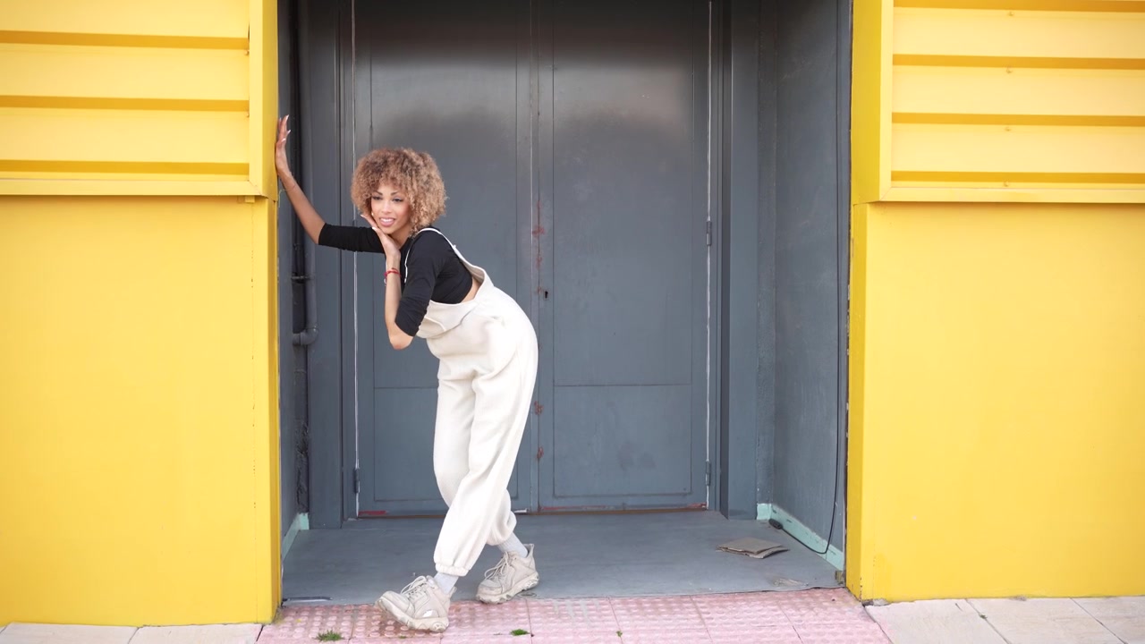 Giovane donna elegante che posa con grazia in un outfit alla moda davanti a un ingresso urbano colorato.