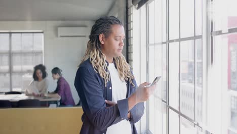 Busy-biracial-male-creative-using-smartphone,-with-colleagues-talking-in-background,-slow-motion