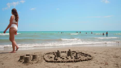 beautiful blonde girl wearing a white bikini strolling along the shore in the summer while beautiful quiet waves roll in