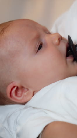 tiny newborn is waved in mom's hands. baby boy suckling a pacifier and looking at mom. close up. vertical video