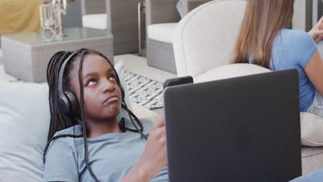 thoughtful diverse teenage female friends with headphones using smartphones and laptop