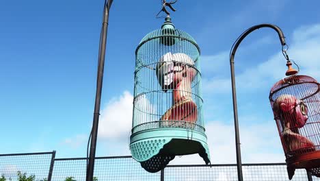 Low-angle-shot-of-vintage-old-ragdoll-mannequines-inside-a-cages-hanging-outside-with-the-view-of-blue-sky-in-the-background-on-a-bright-sunny-day