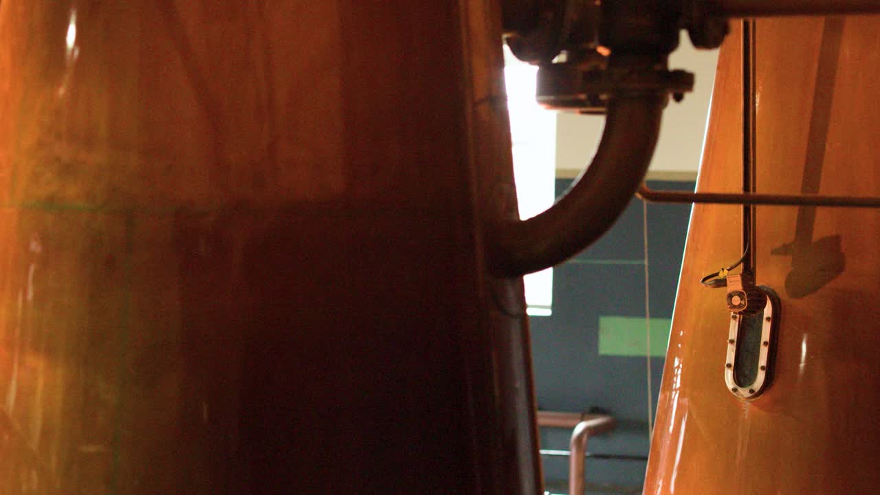Slow pan across copper pot stills inside distillery, warm lighting, industrial environment, smooth camera movement