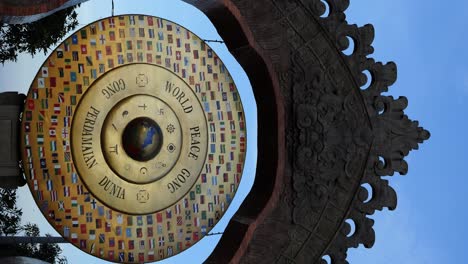 Tiro-Vertical-De-Carro-En-Cámara-Lenta-Que-Captura-El-Gong-De-La-Paz-Mundial-En-Bali,-Un-Faro-Para-La-Paz-Mundial,-Adornado-Con-Banderas-Nacionales-Y-Símbolos-Religiosos