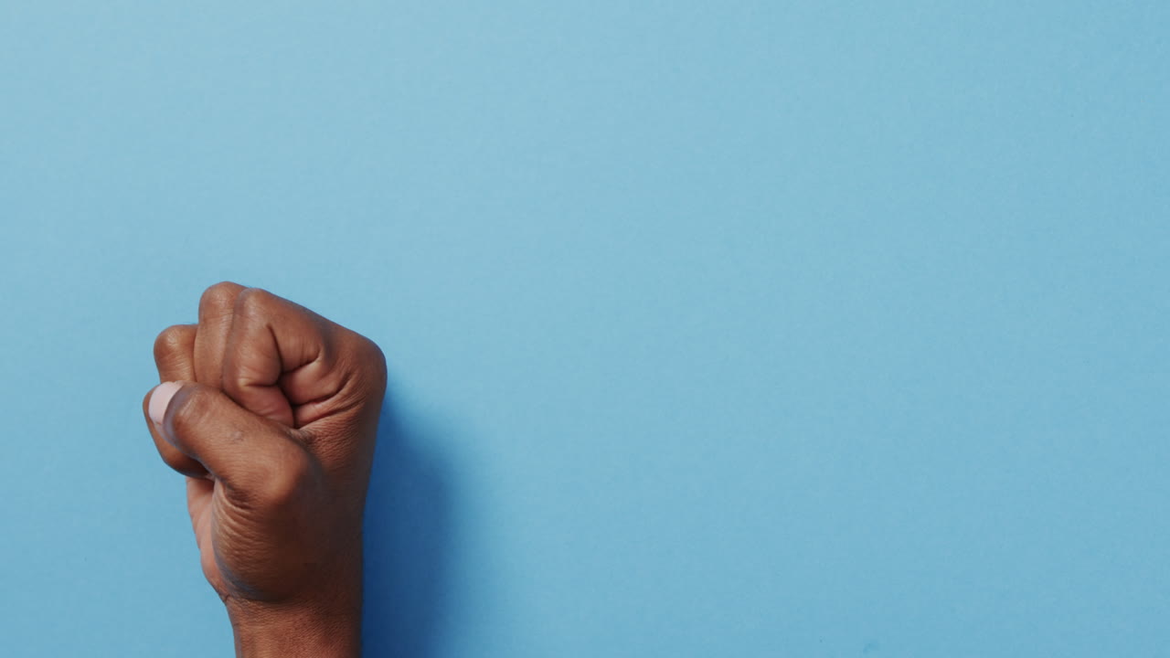 Close up of hand of biracial man making peace sign with copy space on blue background