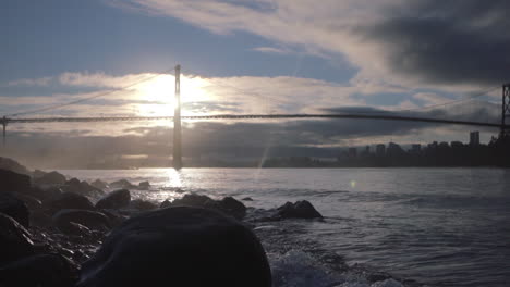 Morgendliche-Meereswellen-Spritzen-Auf-Felsen-Mit-Der-Löwentorbrücke-Im-Hintergrund