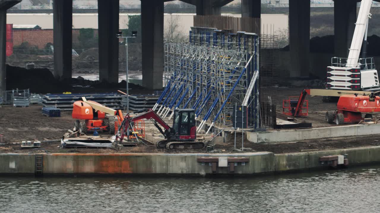 Wide shot of heavy machinery and scaffolding for building a bypass flyover at an urban canal site