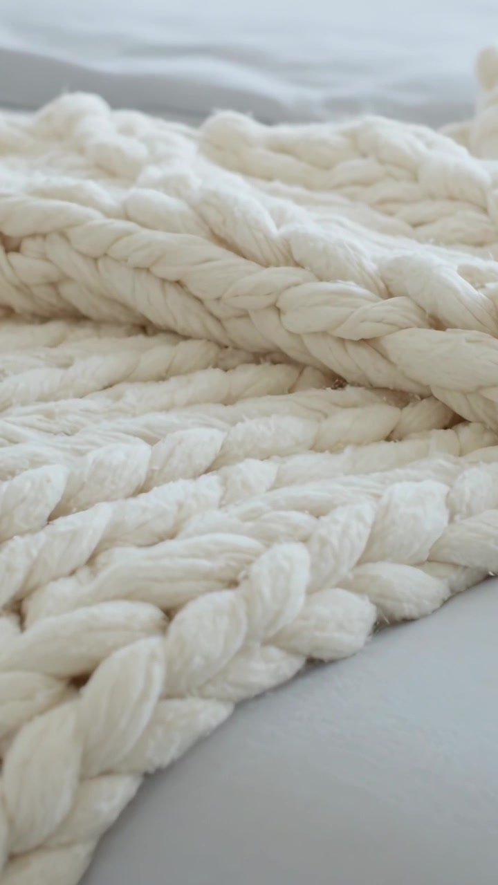 Video verticale: Telecamera che si muove su una spessa coperta di maglia color crema sul letto, rivelando trecce per la trama.