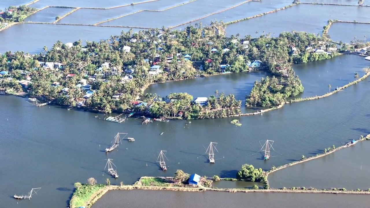 Rekaman drone menangkap keindahan tenang Kadamakkudy dengan kebun kelapa yang rimbun, jalan lintas yang berkelok-kelok, dan laguna air payau yang luas membentang menuju cakrawala yang jauh dalam lanskap tropis
