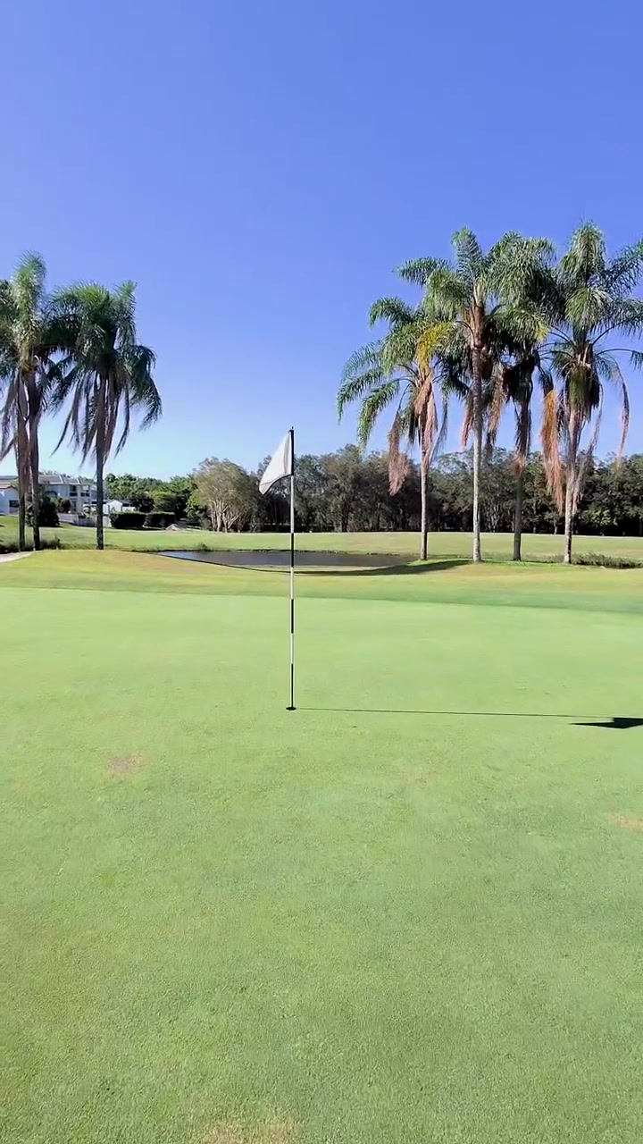 Kameraet beveger seg mot golfhullflagget på en solrik Gold Coast-green med palmetrær