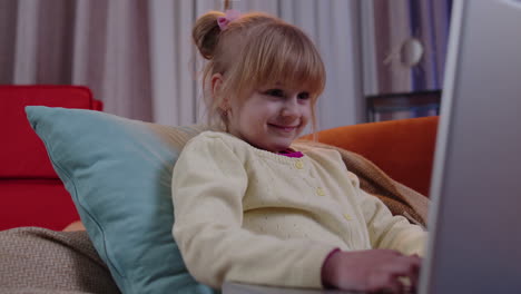 niña pequeña de escuela que usa una computadora portátil aprende a leer lecciones de educación en línea sola en casa