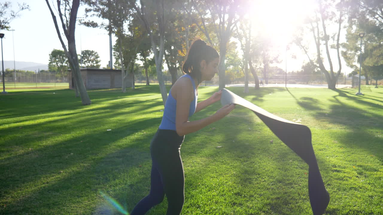 una joven sana desenrollando su alfombra de yoga en un parque soleado para relajarse en meditación pacífica