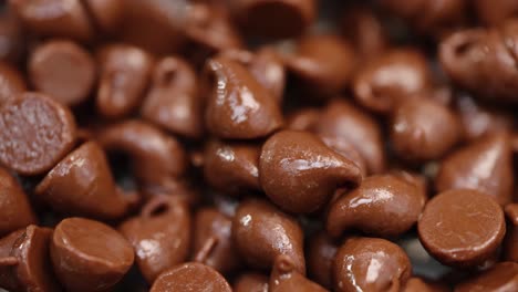 Stack-of-warm-milk-chocolate-chips-glistening-in-light-macro-close-up-4k-light-sweeping-and-pan-right