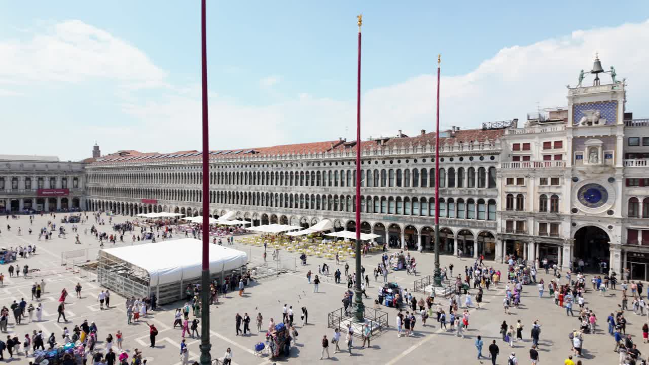 People walk through St. Mark's Square on a sunny day with historic architecture in the background