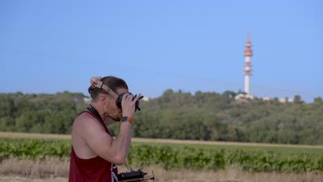 long-haired young man equips mink goggles to control fpv drone, towering red telecom network tower in the background