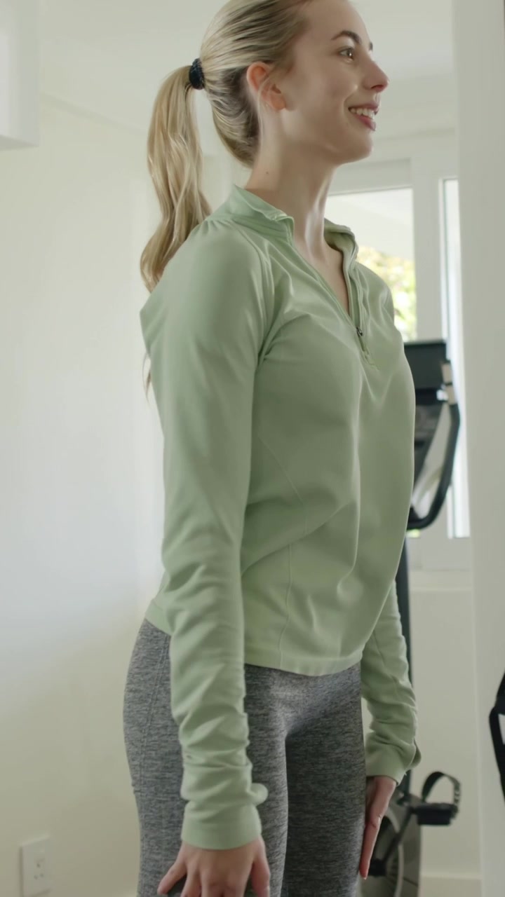 Vertical video: Warming-up woman doing chest and shoulder rolls in home gym with machine in green