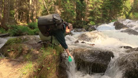 female traveler with a backpack, drinking water in nature in the forest near a mountain river.