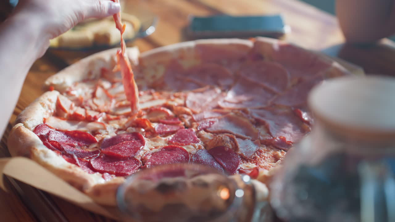 Close up of people enjoying pizza together, hand reaching for a slice, capturing a delicious moment of shared food and happiness, warm indoor setting with vibrant pizza toppings and cozy atmosphere