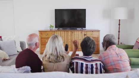 Two-diverse-senior-couples-sitting-on-a-couch-watching-a-game-drinking-beer-cheering