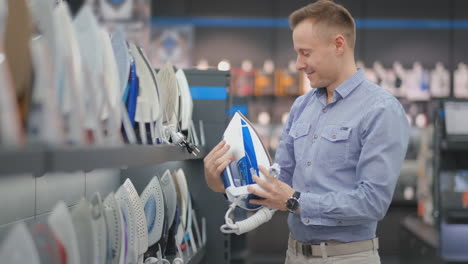 un joven apuesto con una camisa elige una plancha en una tienda de electrónica de consumo.