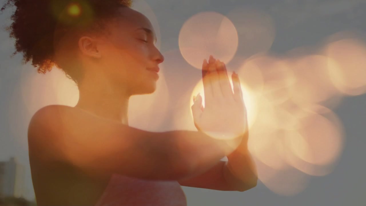 Woman starting raised arms, lowering into prayer pose at shore for wellness bokeh revealing face