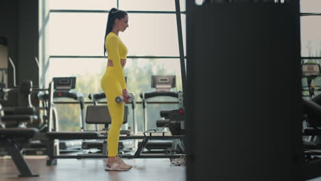 fit hispanic woman performing weight lifting deadlift exercise with dumbbell at gym in yellow sportswear. woman brunette fitness performing doing deadlift exercise with dumbbell