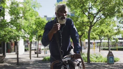 hombre mayor afroamericano sentado en una bicicleta con auriculares en el camino