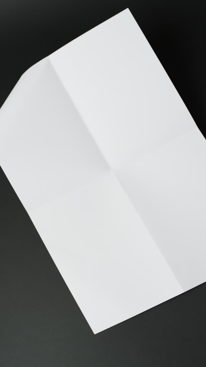 Vertical video of piece of white paper with creases on black background