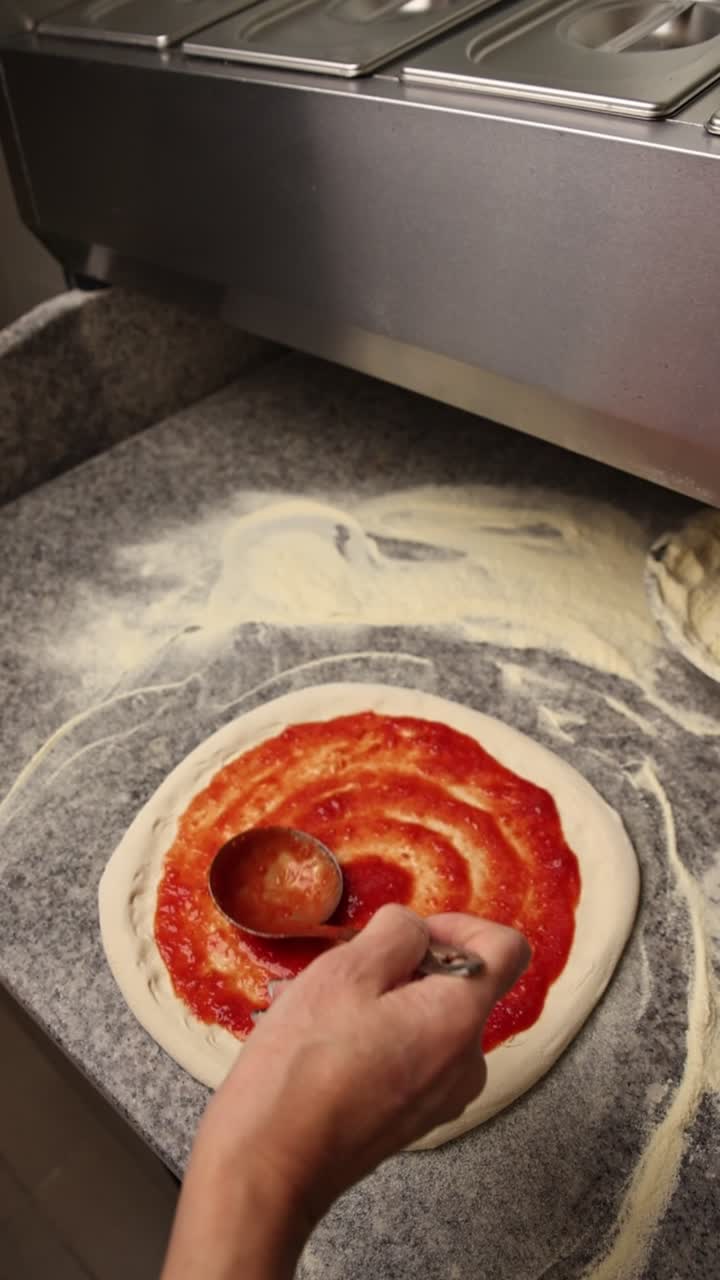 Close-up de mão espalhando molho de tomate na massa de pizza