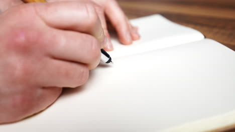 young male hands close up while open new paper notebook with blank pages writing new idea and creativity concepts with ink pen