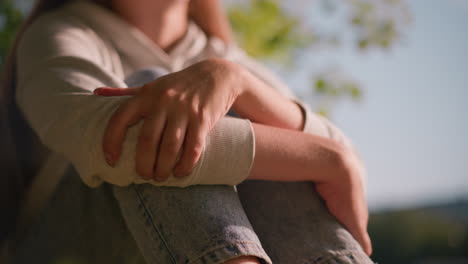 close-up of young woman s arms folded over knees, hands gently resting, with sunlight casting soft highlights, casual attire with blurred natural background