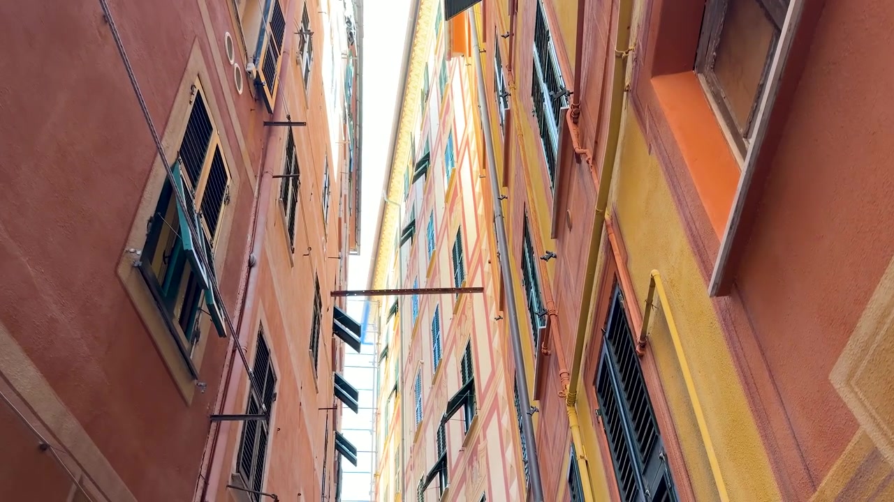 Uma perspectiva em ângulo baixo atravessa um beco estreito entre edifícios de apartamentos mediterrâneos altos e vibrantes.
