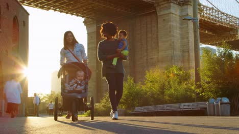 two mothers with toddlers walking under bridge in manhattan