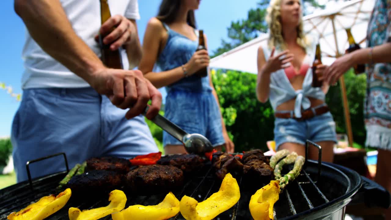 Group of friends having a bottle of beer while preparing barbeque