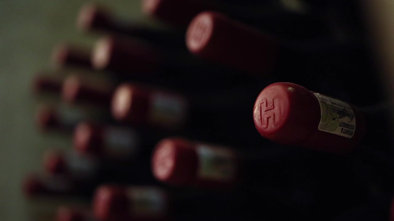Botellas de vino tinto en estante, enfoque selectivo en tapones de cera sellados, detalle en primer plano.