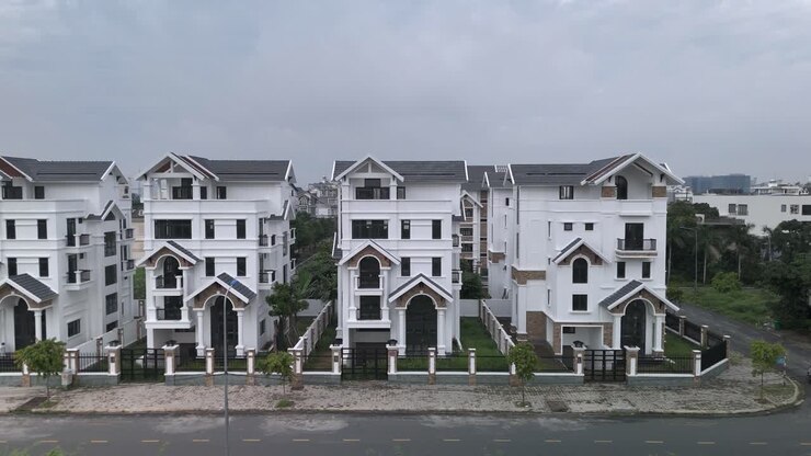 A newly constructed row of identical large white multi story villa styled houses along a suburban road