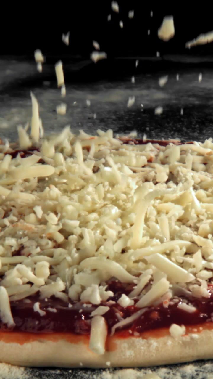 Mozzarella grattugiata che cade su una pizza con salsa di pomodoro al rallentatore