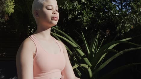 focused biracial woman practicing yoga and meditating in garden in slow motion