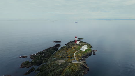 aerial establishing shot of a red and white striped lighthouse in norway