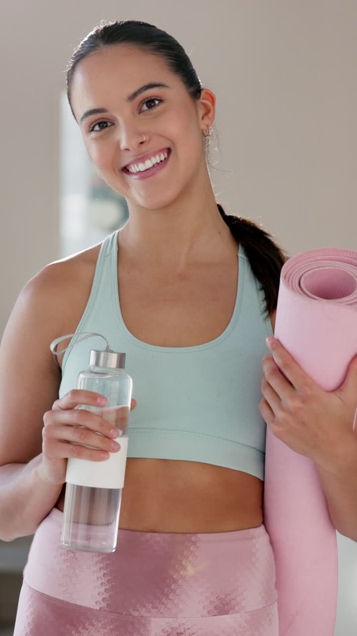 mujer sonriente con equipo de fitness sosteniendo una alfombra de yoga y una botella de agua