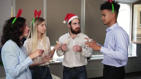 young attractive african man telling his story during corporate christmas party in the office. multiracial group of happy office