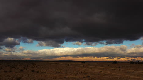 menacing dark clouds fill the sky just before a violent cloudburst in the mojave desert - sliding aerial view