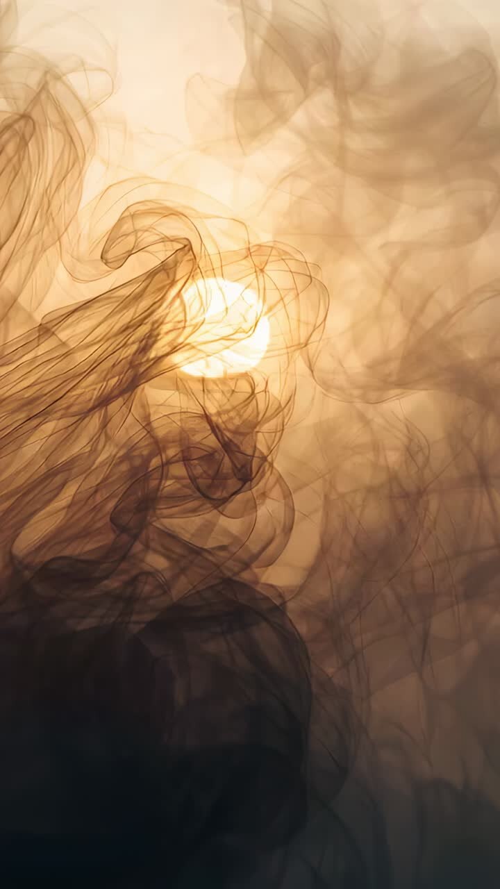 Vertical video: Swirling smoke responding to drafts in dark studio close-up, revealing bright lamp
