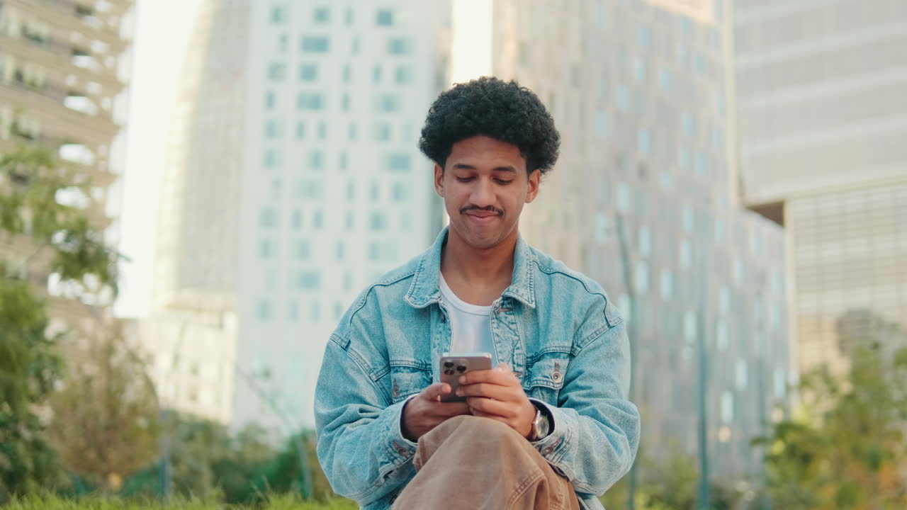 Giovane uomo con capelli ricci che usa lo smartphone in un contesto urbano