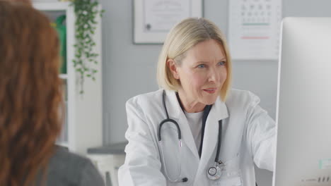 mature female doctor or consultant wearing white coat having meeting with female patient