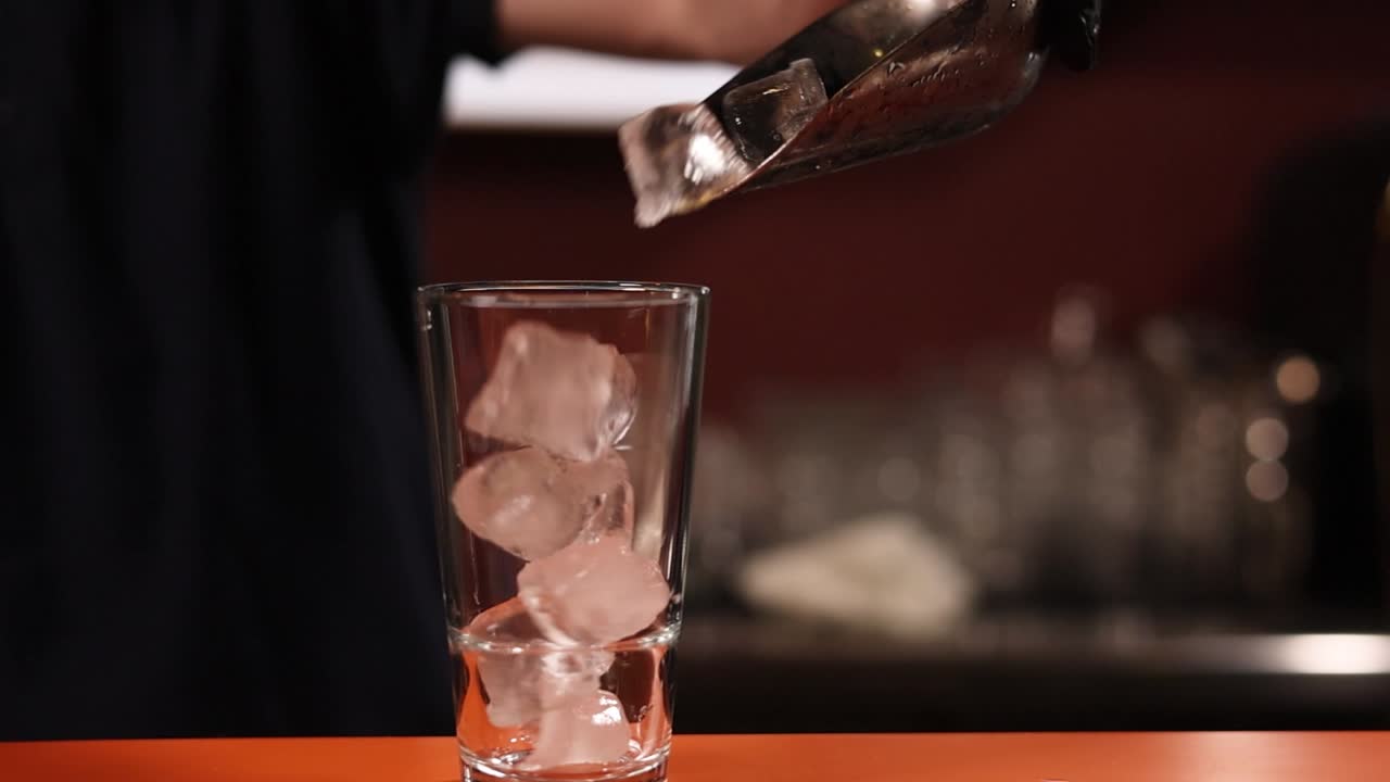 el camarero añadiendo hielo a un vaso de cóctel