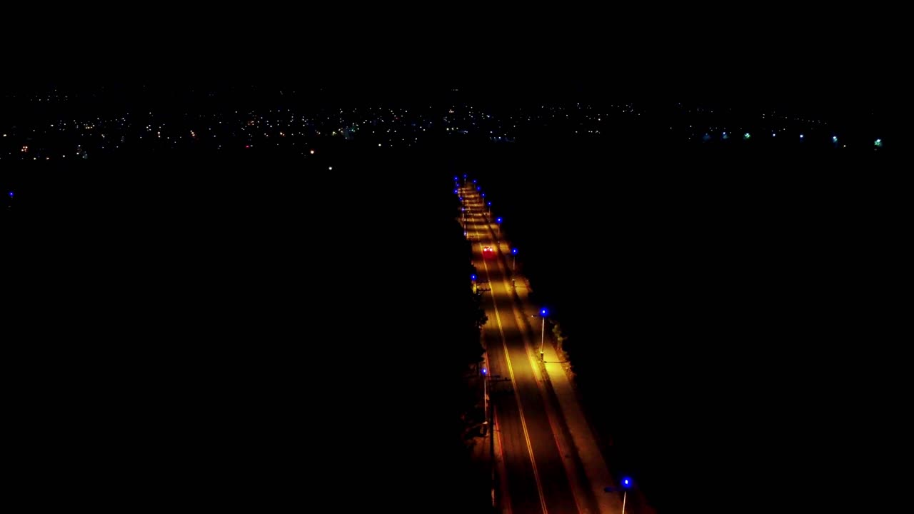 vista nocturna de una carretera iluminada con coches, que se extiende en un paisaje urbano bajo un cielo oscuro, vista aérea