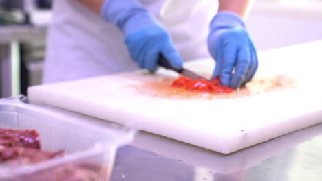 부엌에 있는 나무 탁자에 토마토 조각을 자르는 라텍스 장갑을 낀 사람의 손