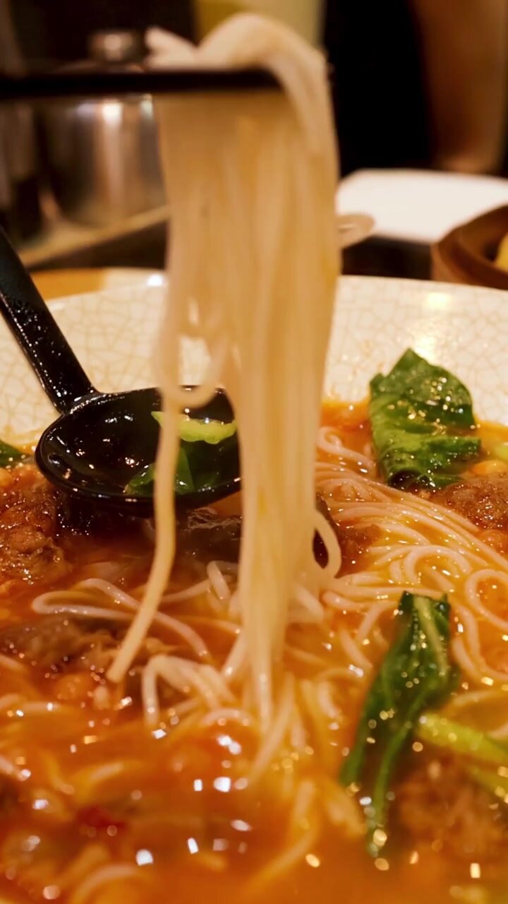 Un primo piano dettagliato di sottili noodles bianchi sollevati da un brodo saporito
