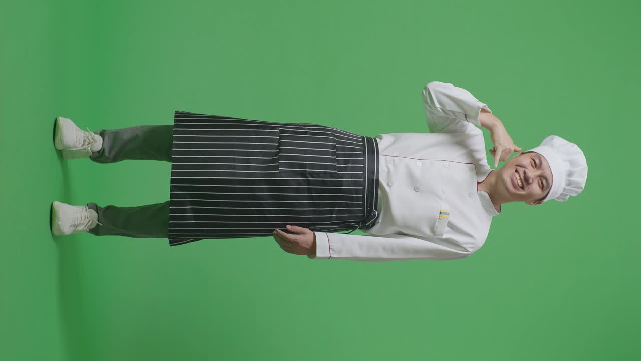 아시아 남자의 몸이 가득 차있는 요리사는 미소 짓고 녹색 스크린 배경 스튜디오에 서있는 동안 카메라에 제스처를 호출합니다.